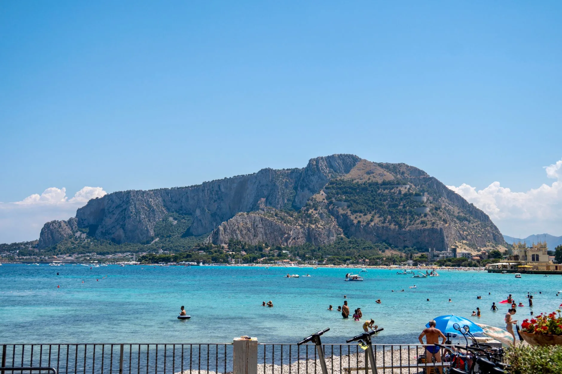 Mondello Beach with clear blue water, beachgoers, and Mount Pellegrino in the background.