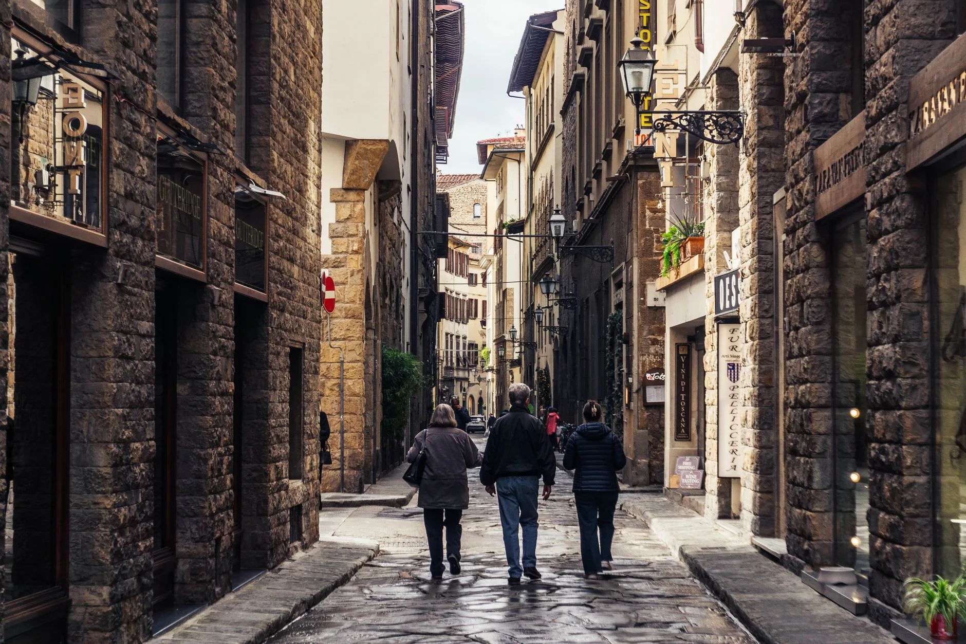 Three people walking along a cobblestone street lined with historic buildings in Florence.