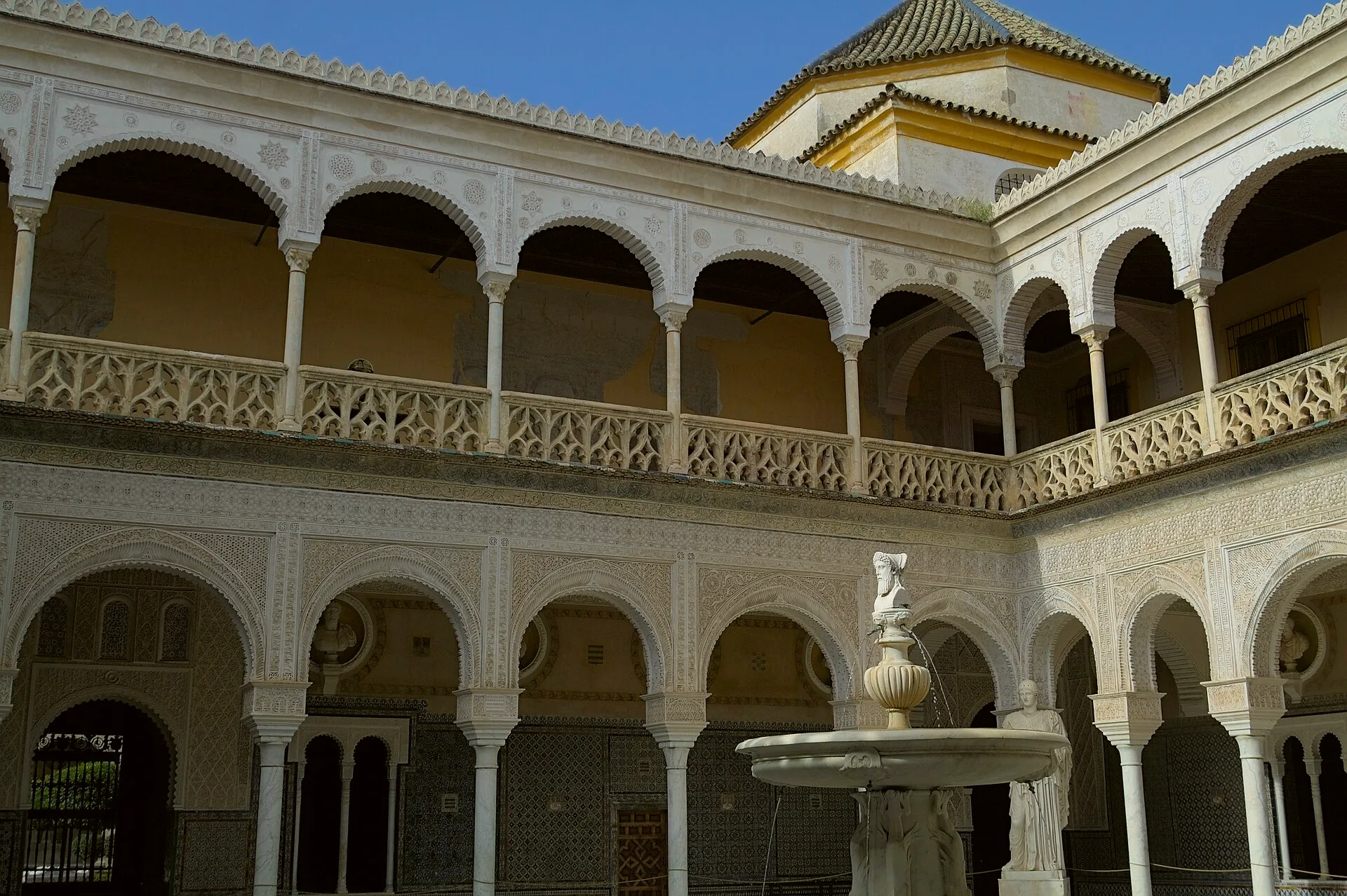 The courtyard at Casa de Pilatos, with a central fountain and sculptures at its corners.