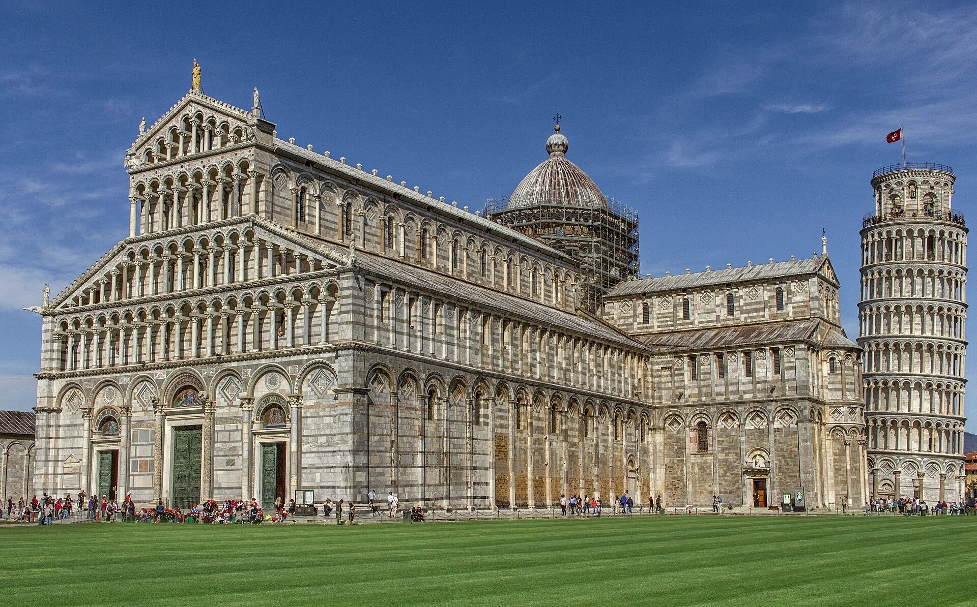 Pisa Cathedral and its bell tower, the Leaning Tower, beside the grass and paving of Piazza del Duomo.