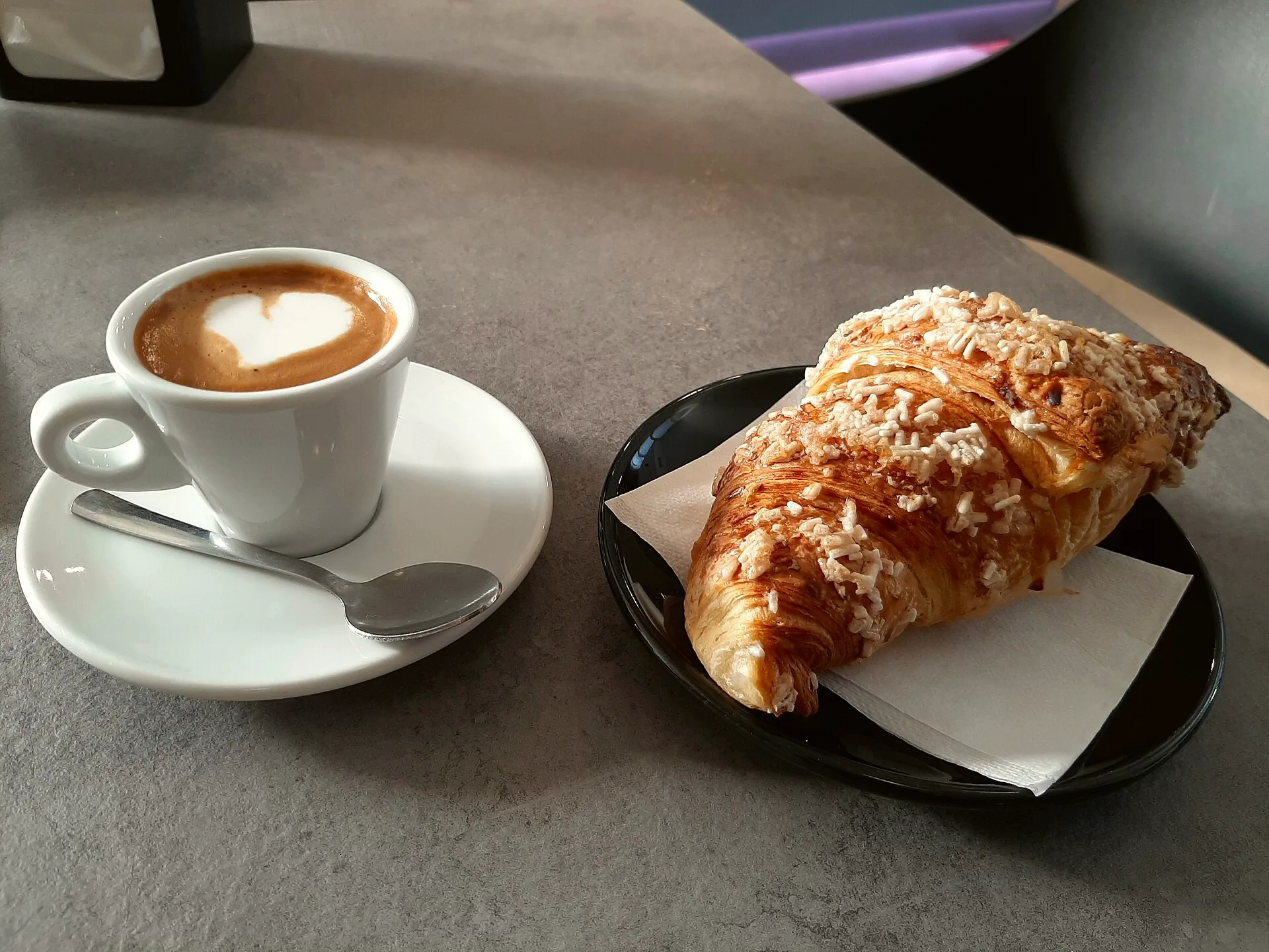 A cornetto beside a cup of cappuccino.