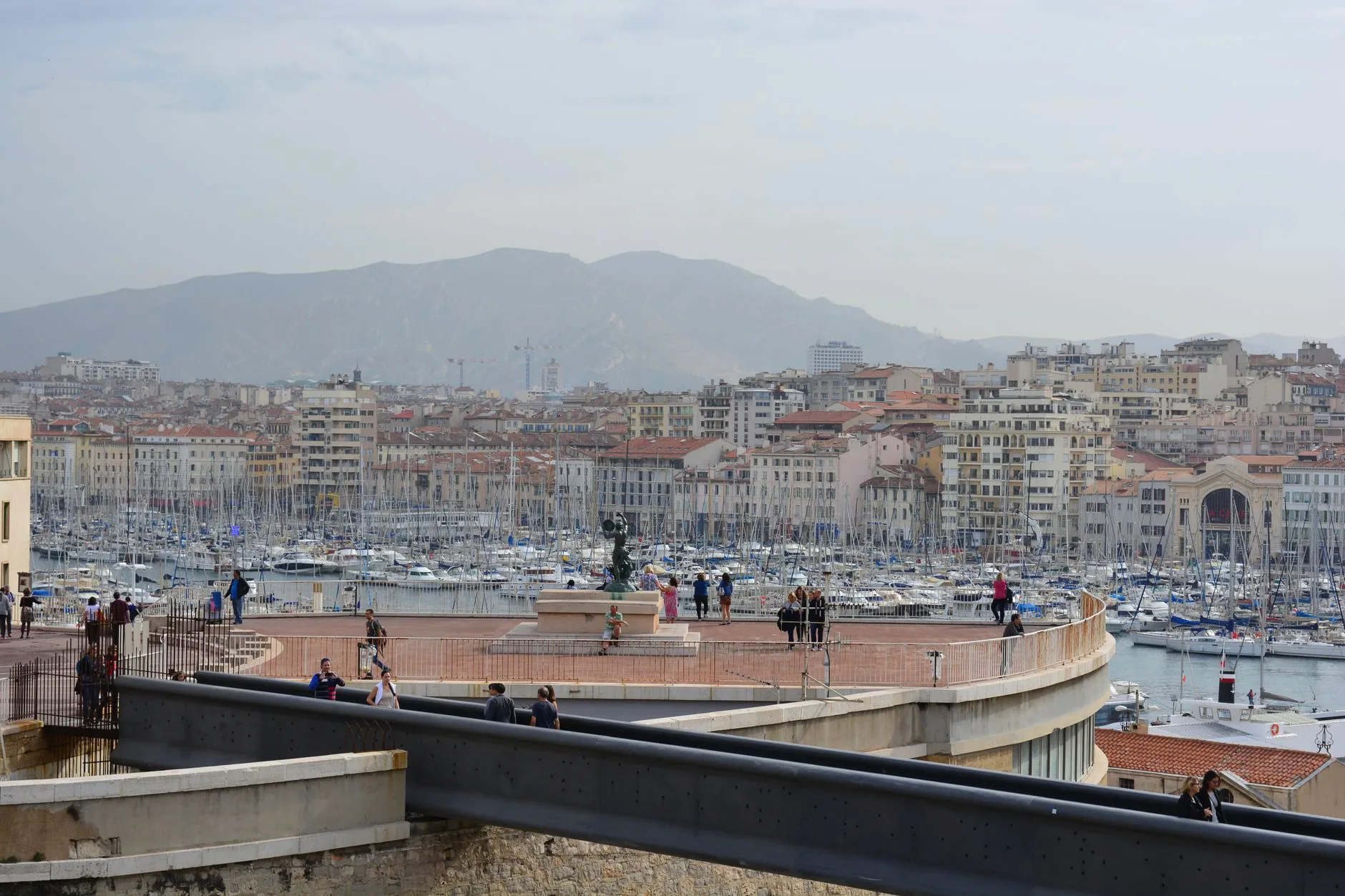 People walking beside the Vieux-Port, with boats in the harbour and Marseille’s skyline beyond.