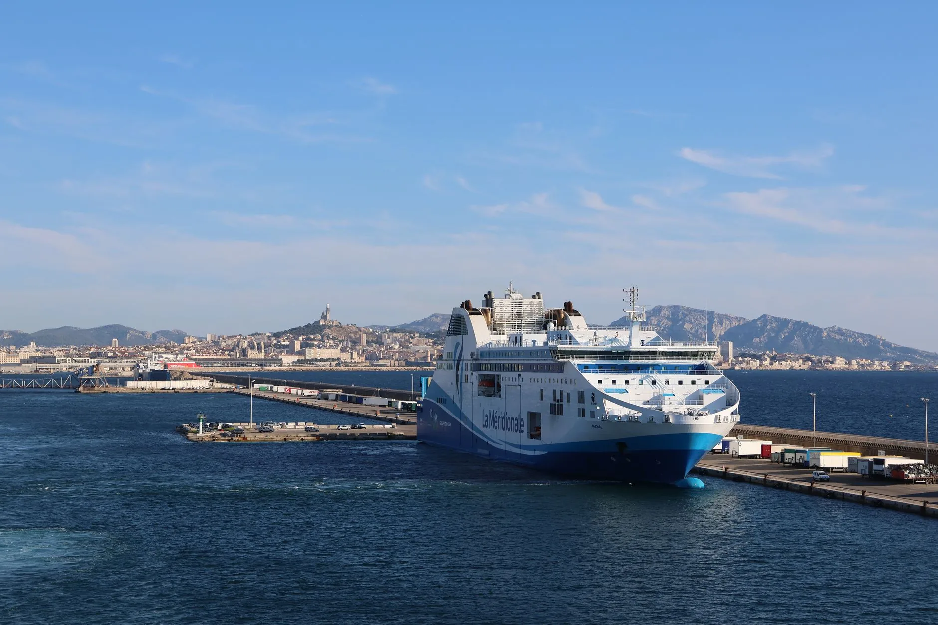 A large ferry docked in Marseille harbour with the city and mountains behind it