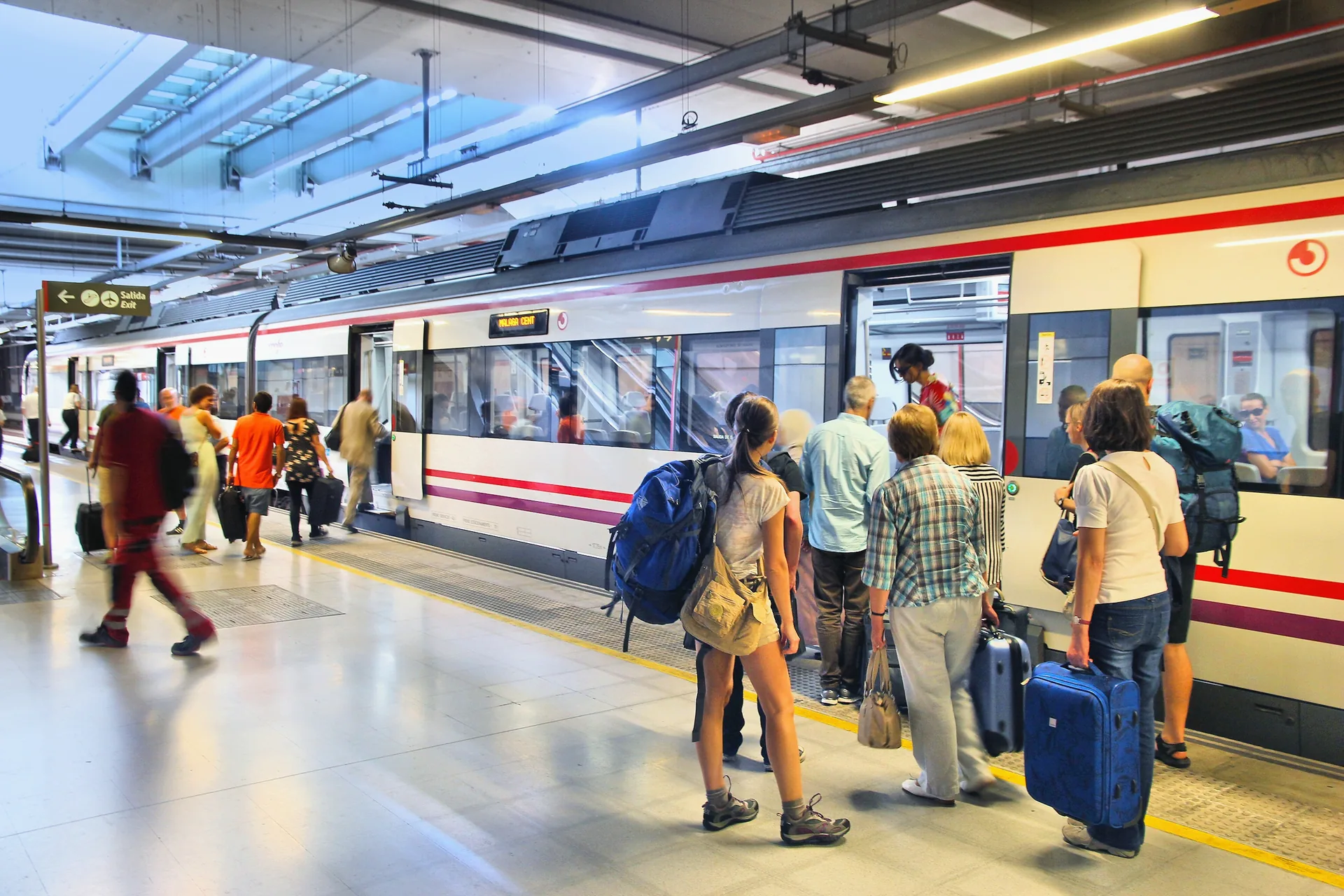 Passengers with suitcases and backpacks boarding a Cercanías Málaga train at Málaga Airport station.