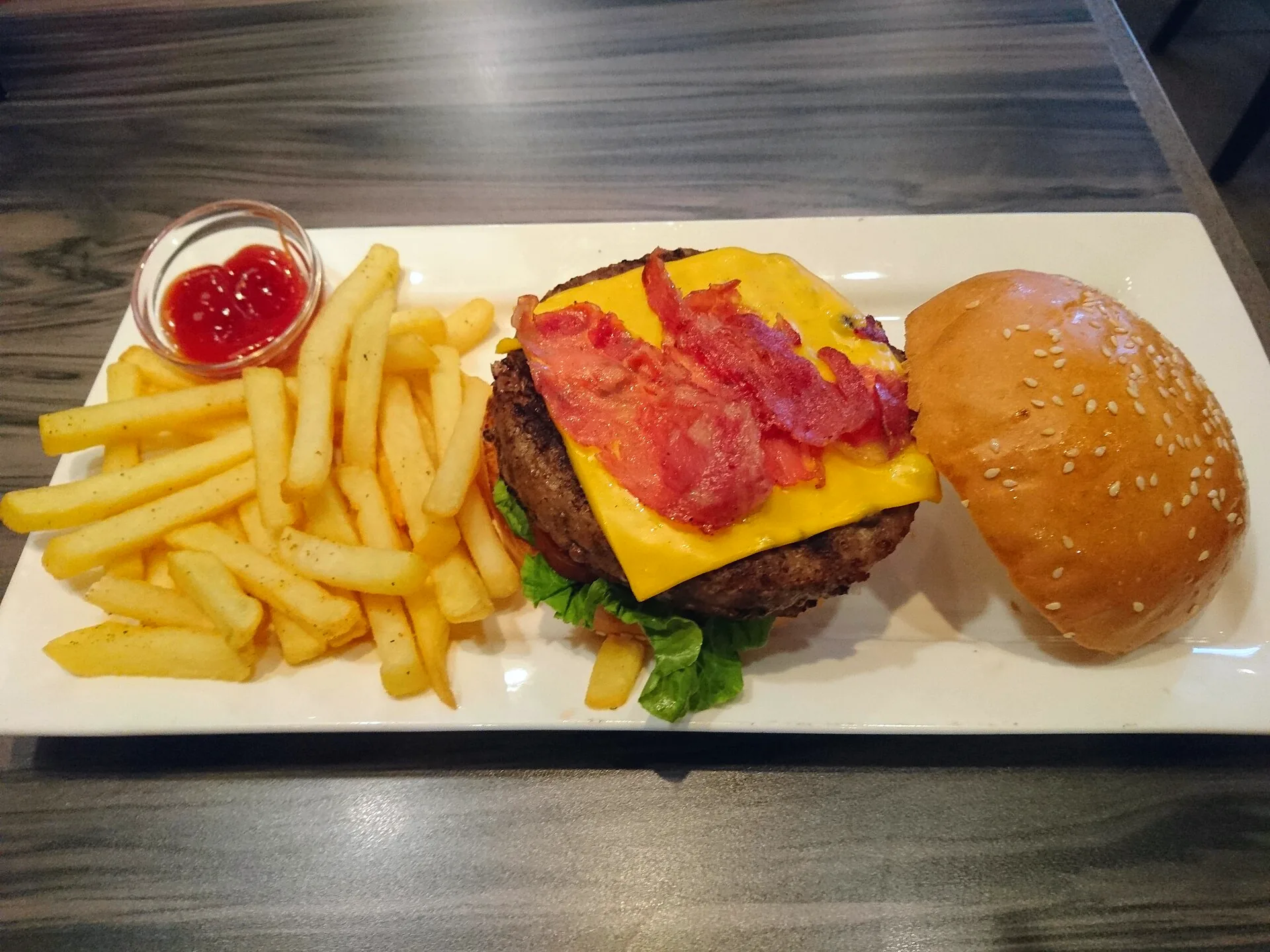 A bacon cheeseburger served with French fries on a plate.