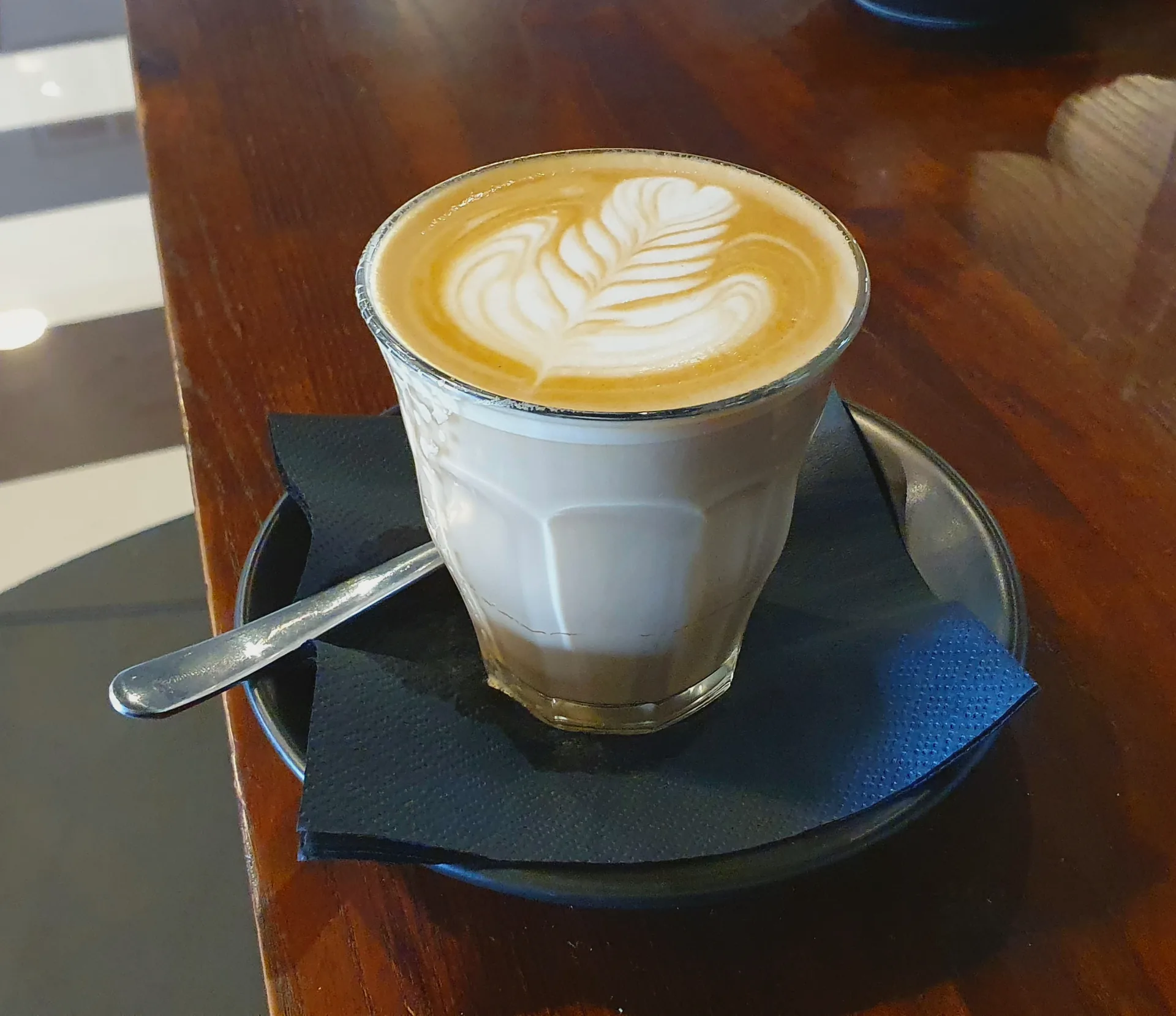 A glass of caffe latte topped with a free-poured microfoam pattern.