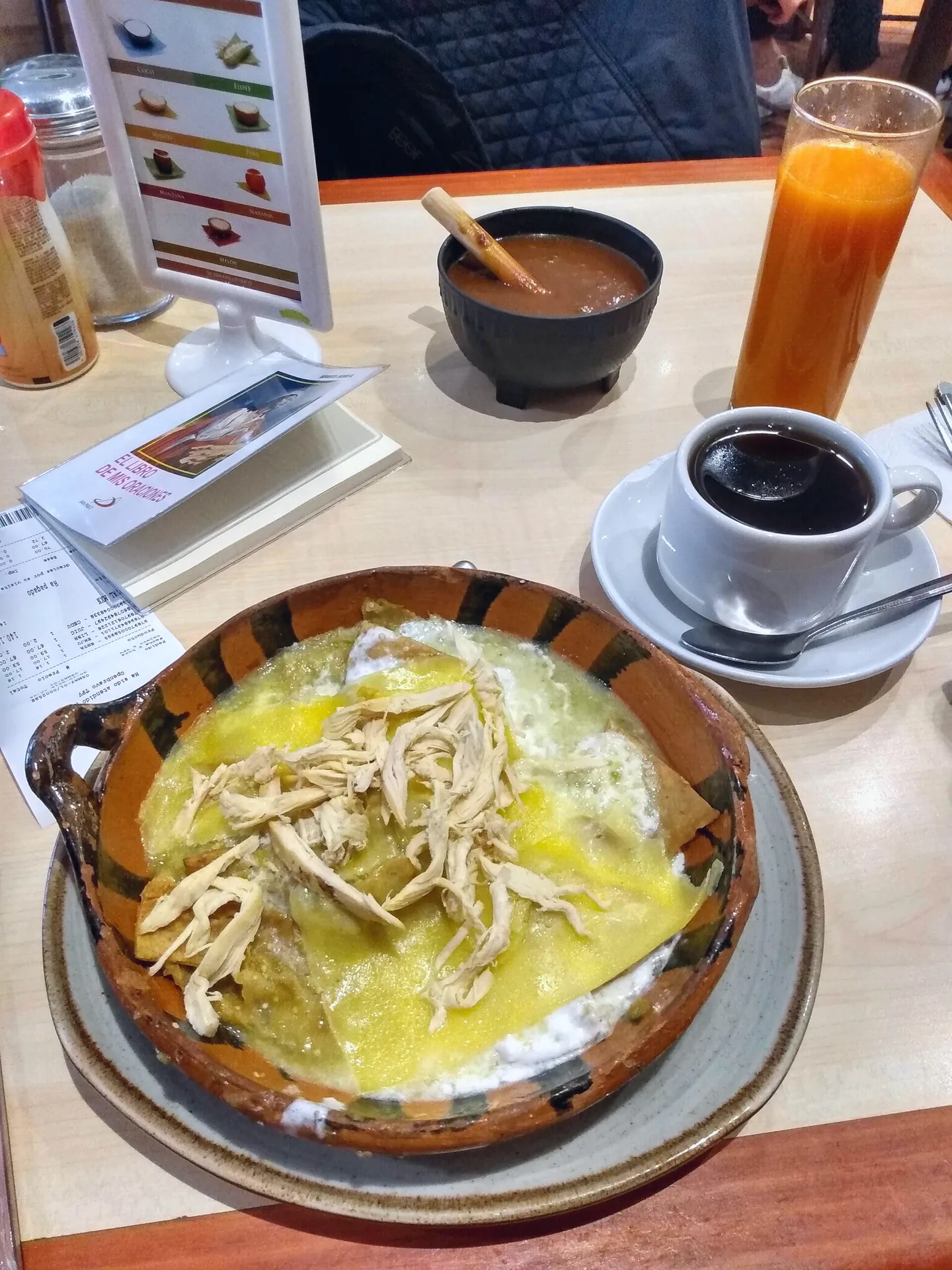 A plate of chicken-topped chilaquiles with coffee and carrot juice.