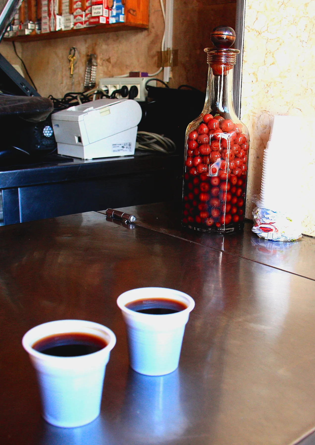 A shot of dark cherry-coloured ginjinha in a plastic glass.