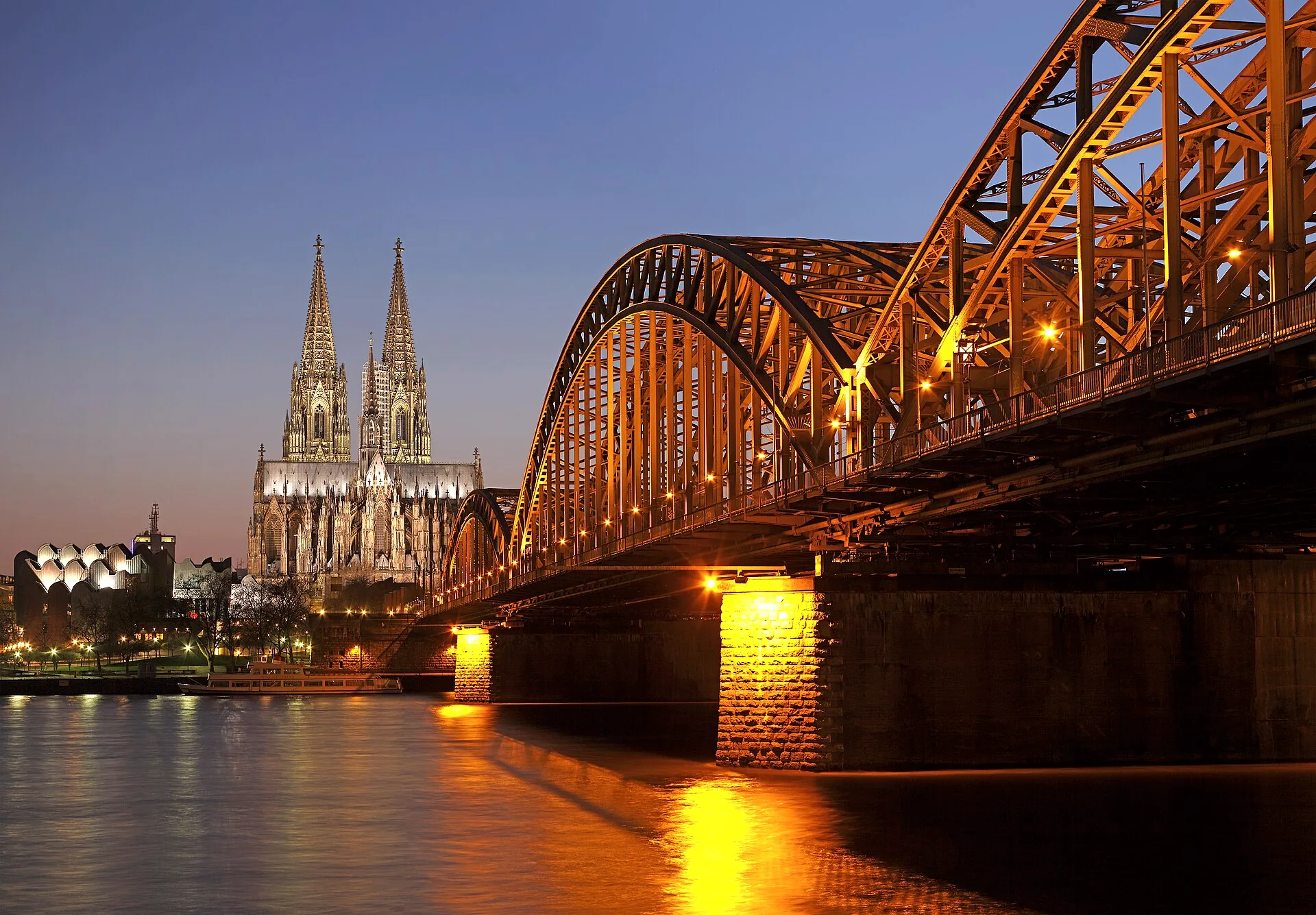 The Hohenzollern Bridge crossing the Rhine, with Cologne Cathedral visible behind it at blue hour.