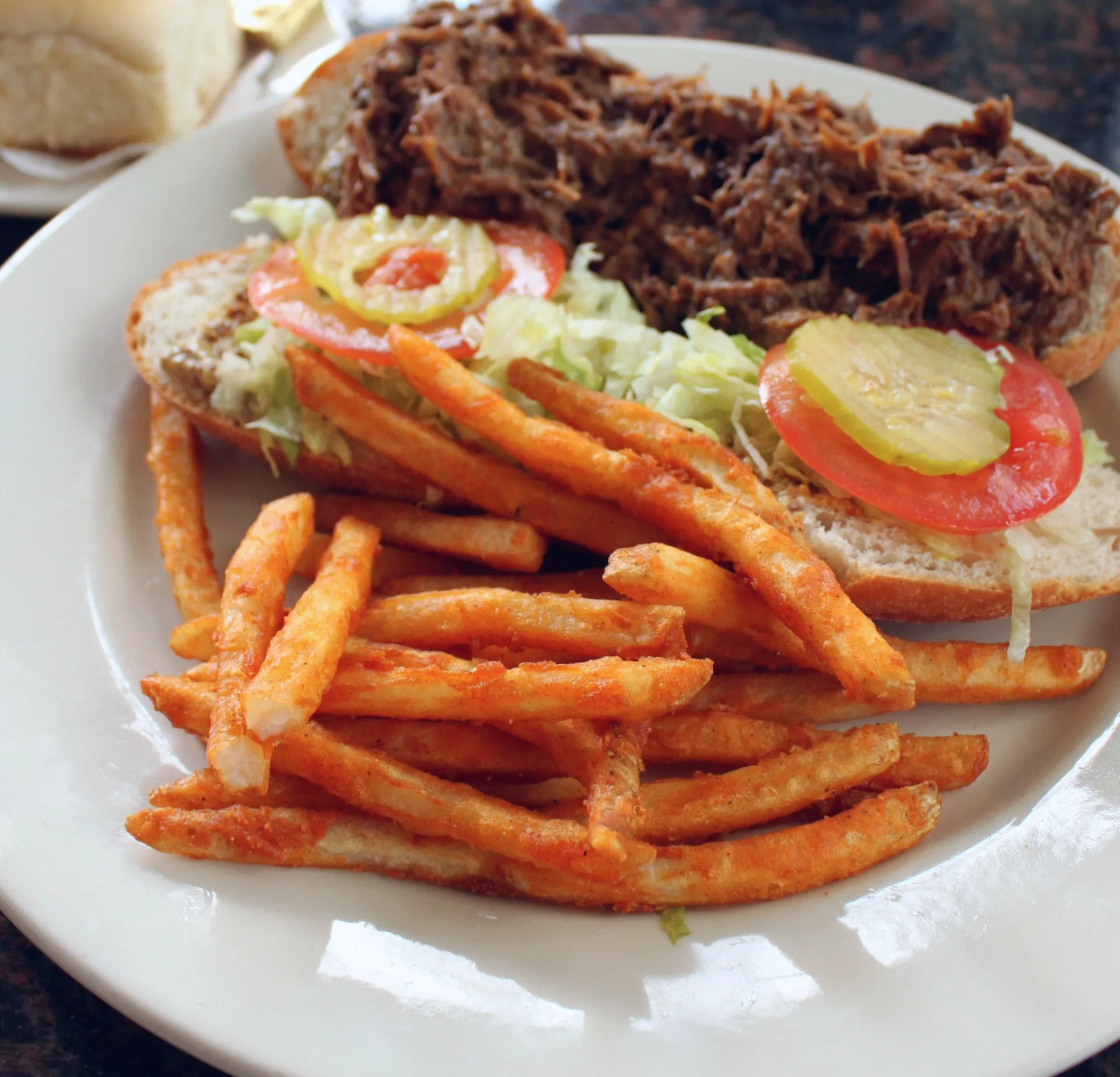 A po’ boy sandwich with fries on a plate.