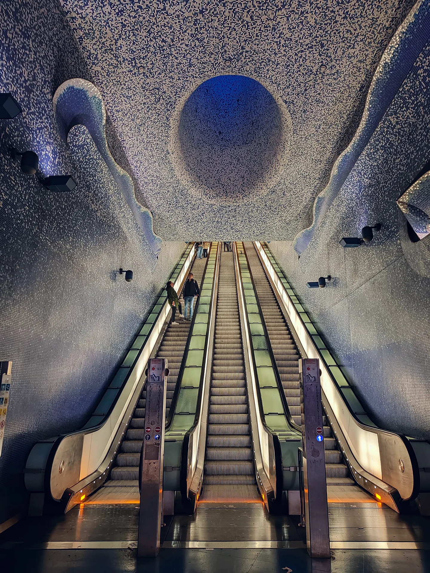 The illuminated interior of Toledo station, with a curved escalator shaft and colourful mosaic walls.