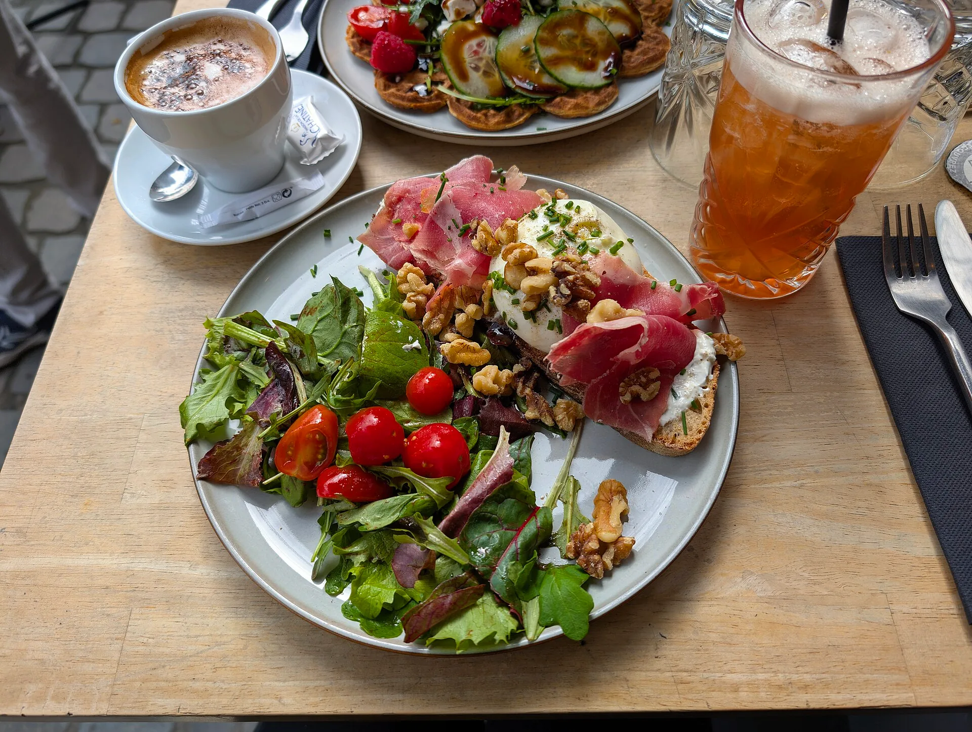 An open tartine topped with mascarpone, Parma ham, mesclun, burrata, basil and walnuts.