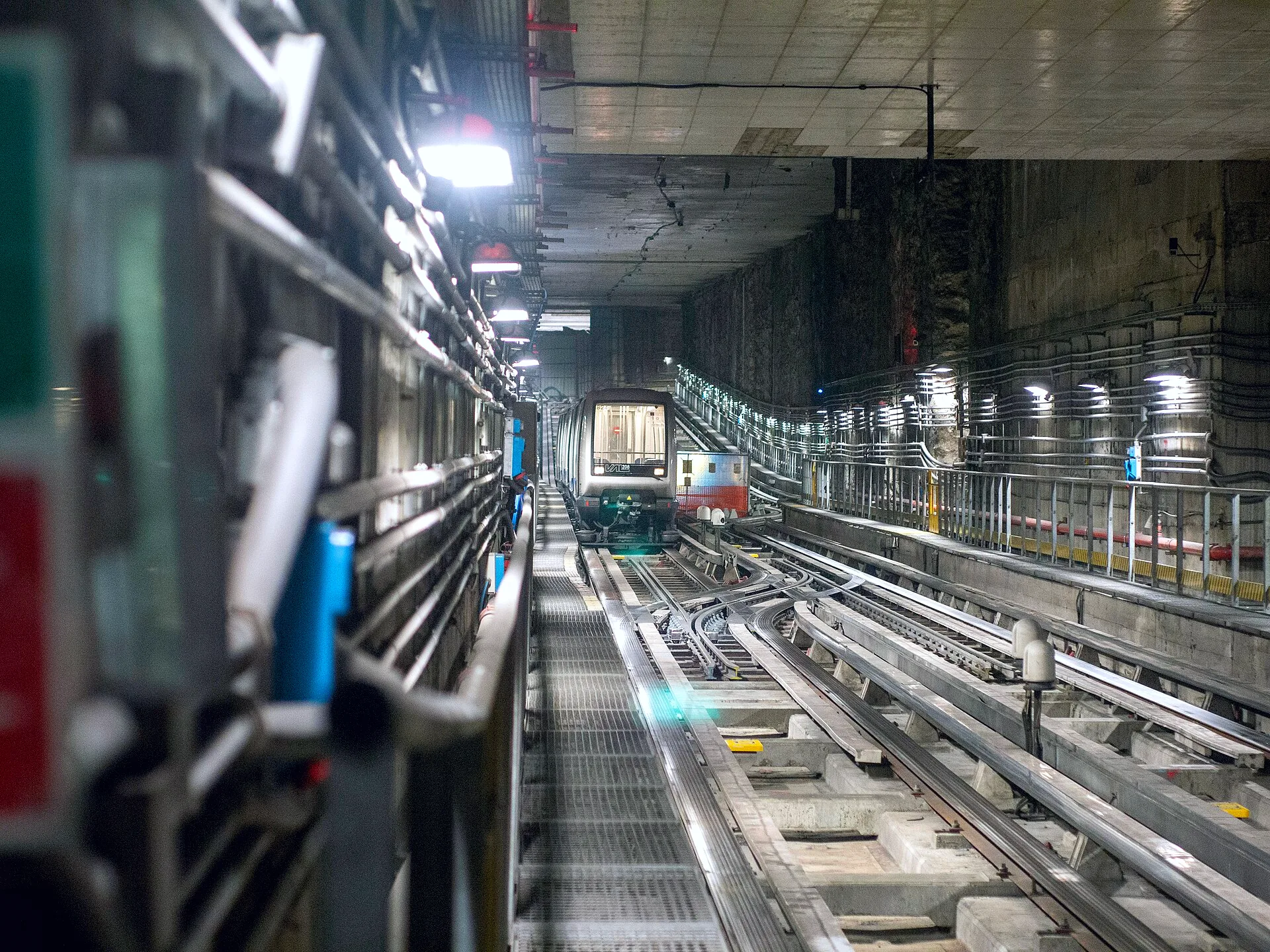 A Turin Metro train on tracks at the Fermi terminal, surrounded by concrete walls and metal grates.