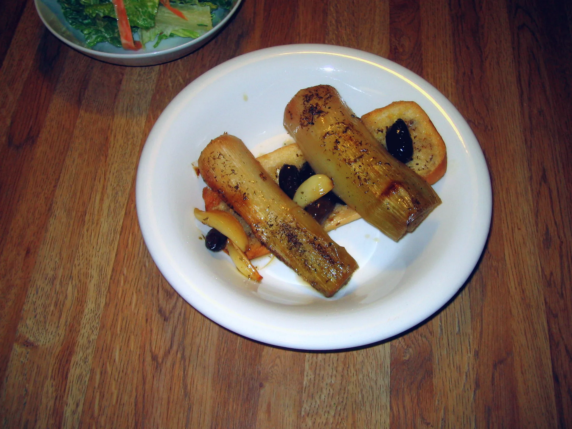 Wine-braised leeks plated with a slice of garlic toast.