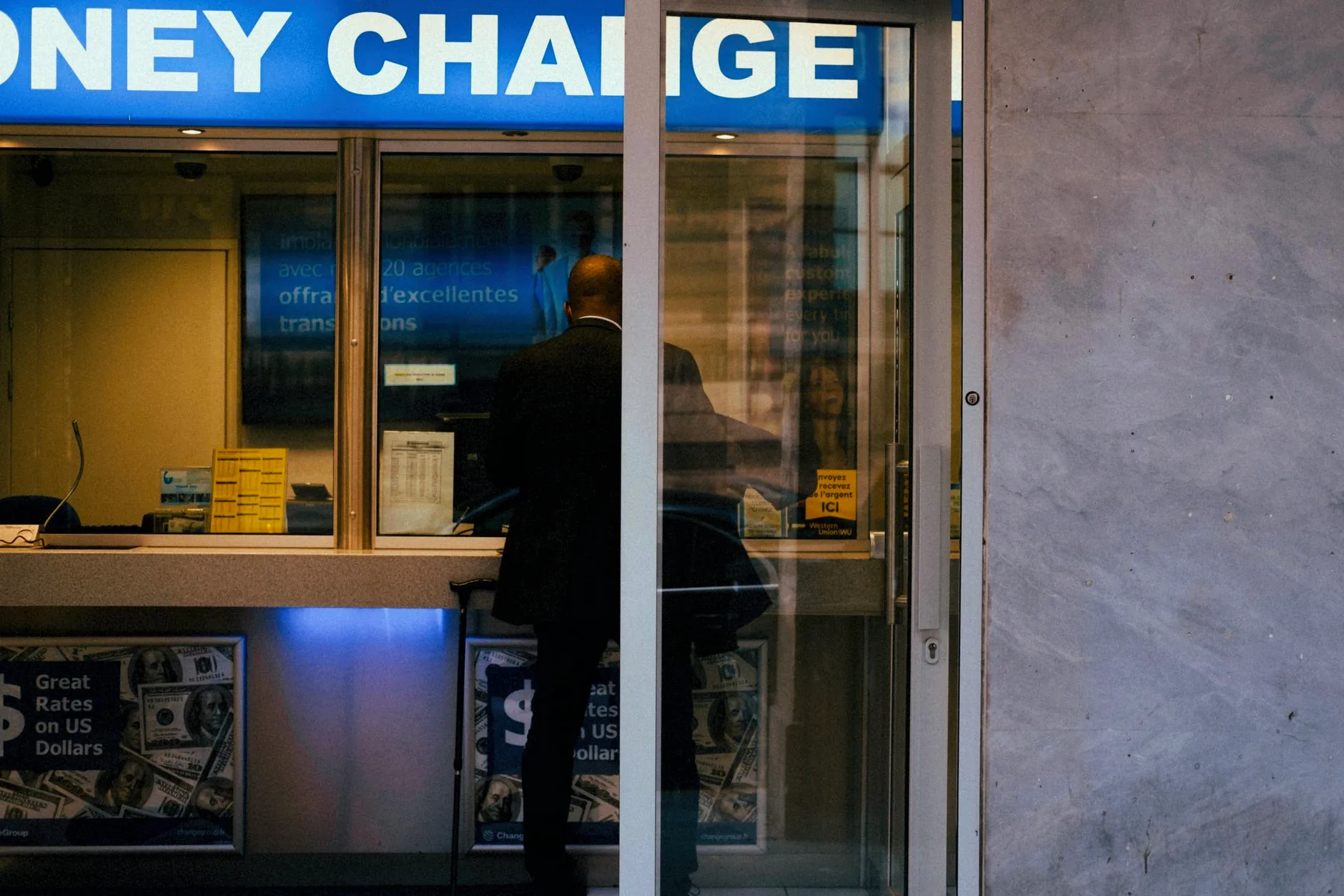 A man at a currency exchange office window beneath posted exchange rates.