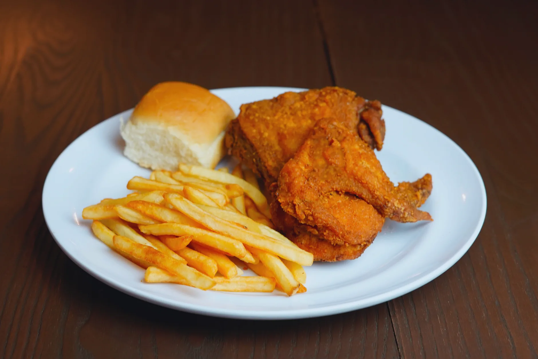 Fried chicken with chips and a bread roll on a white plate.