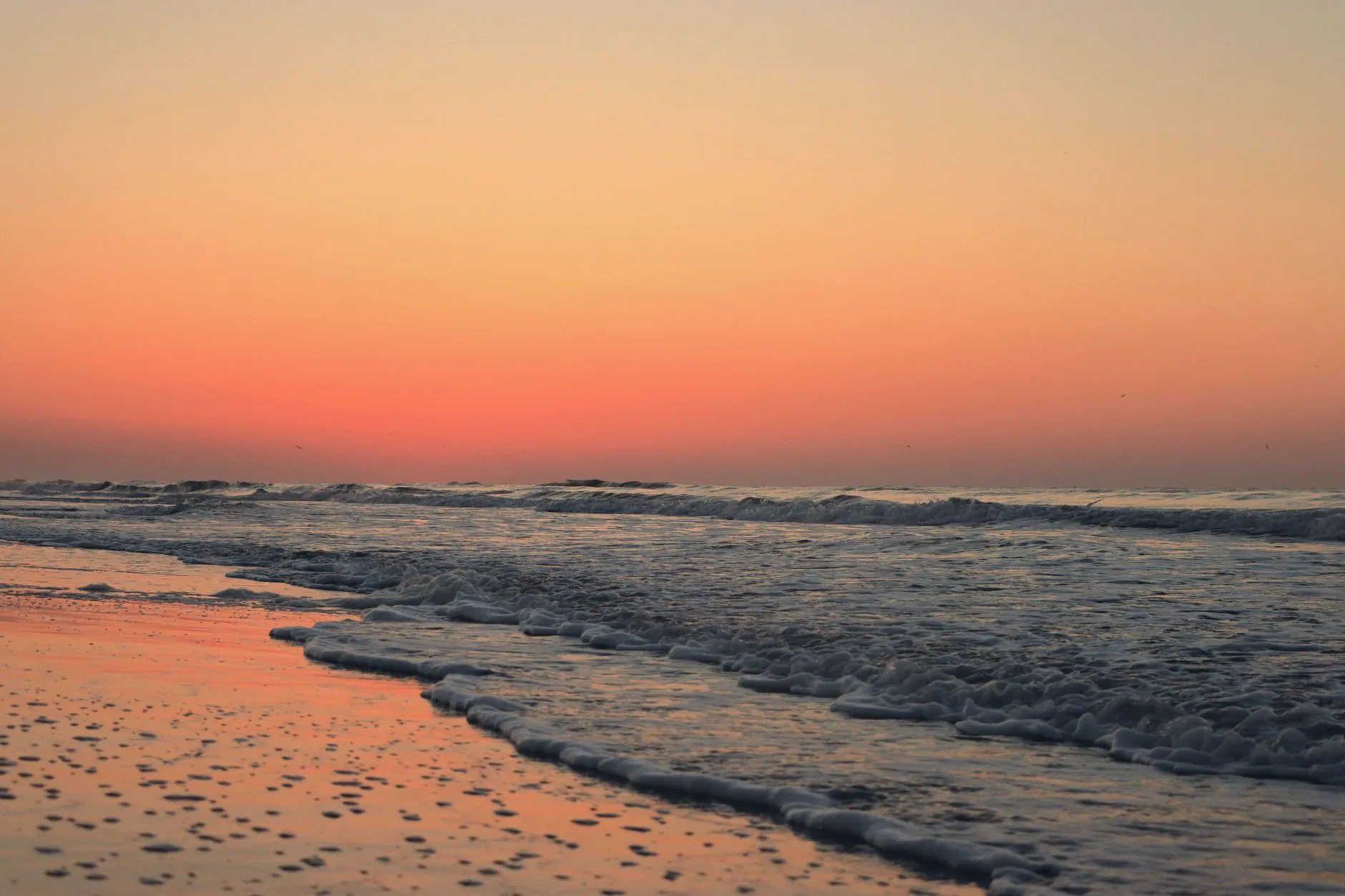Sunrise over the Atlantic Ocean at Coligny Beach, with waves reaching the shore beneath an orange sky.