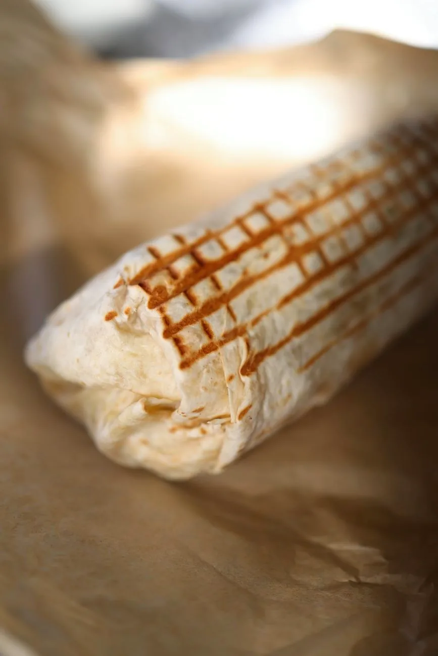 A grilled burrito wrapped in brown paper, shown close up.