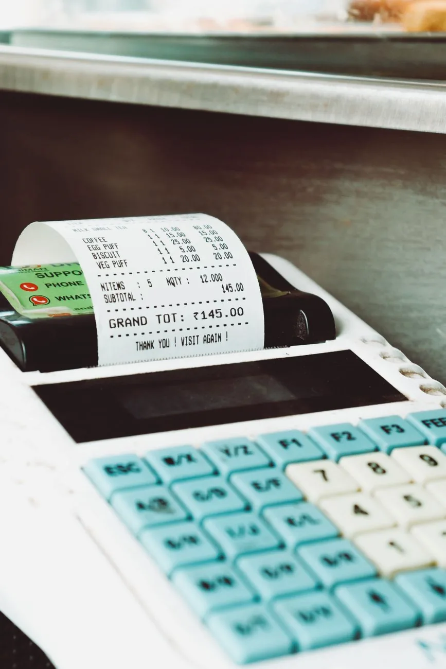 A cash register prints a paper receipt beside a payment card.