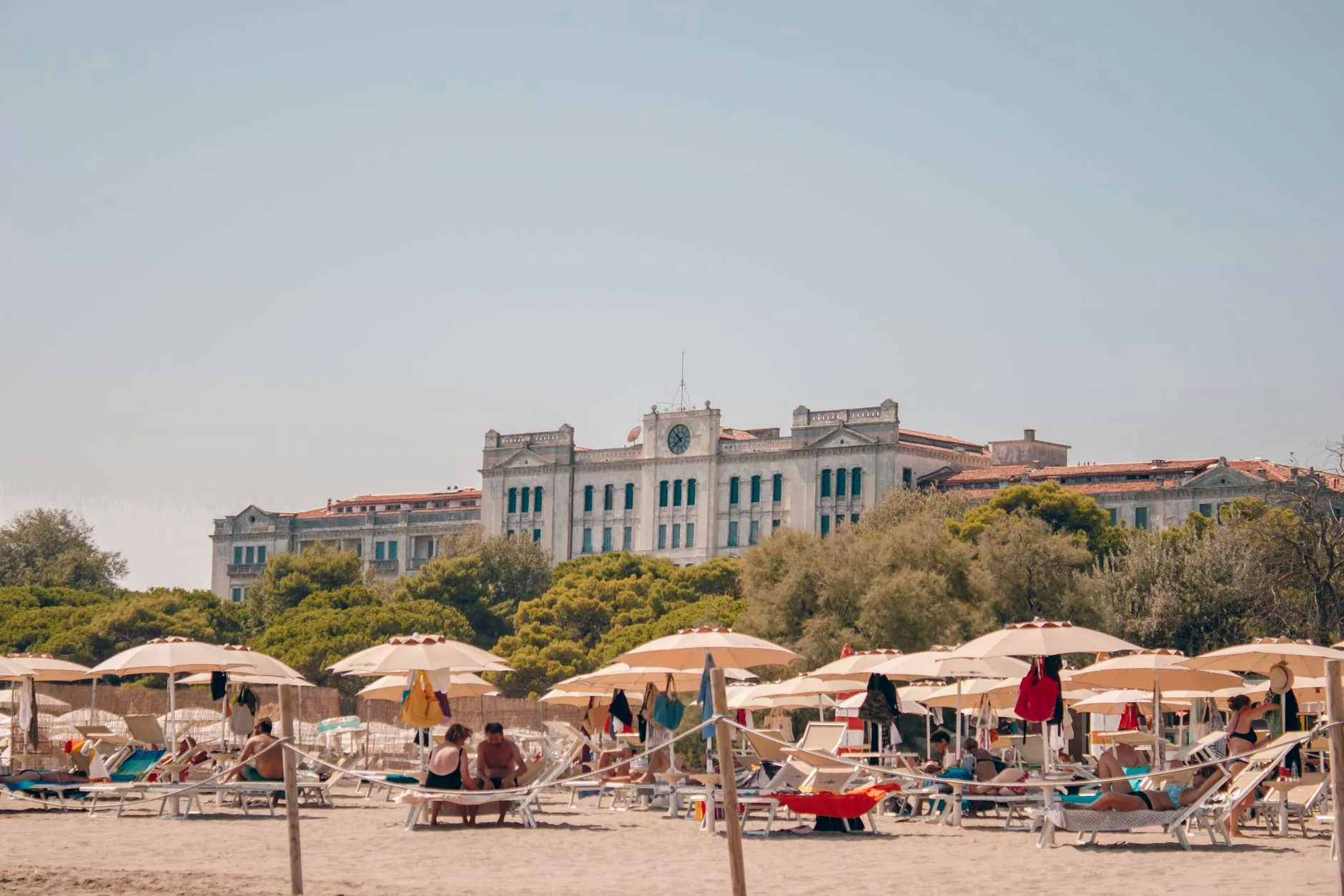 Sandy Venice Lido beach with rows of umbrellas and the Grand Hotel des Bains behind it.