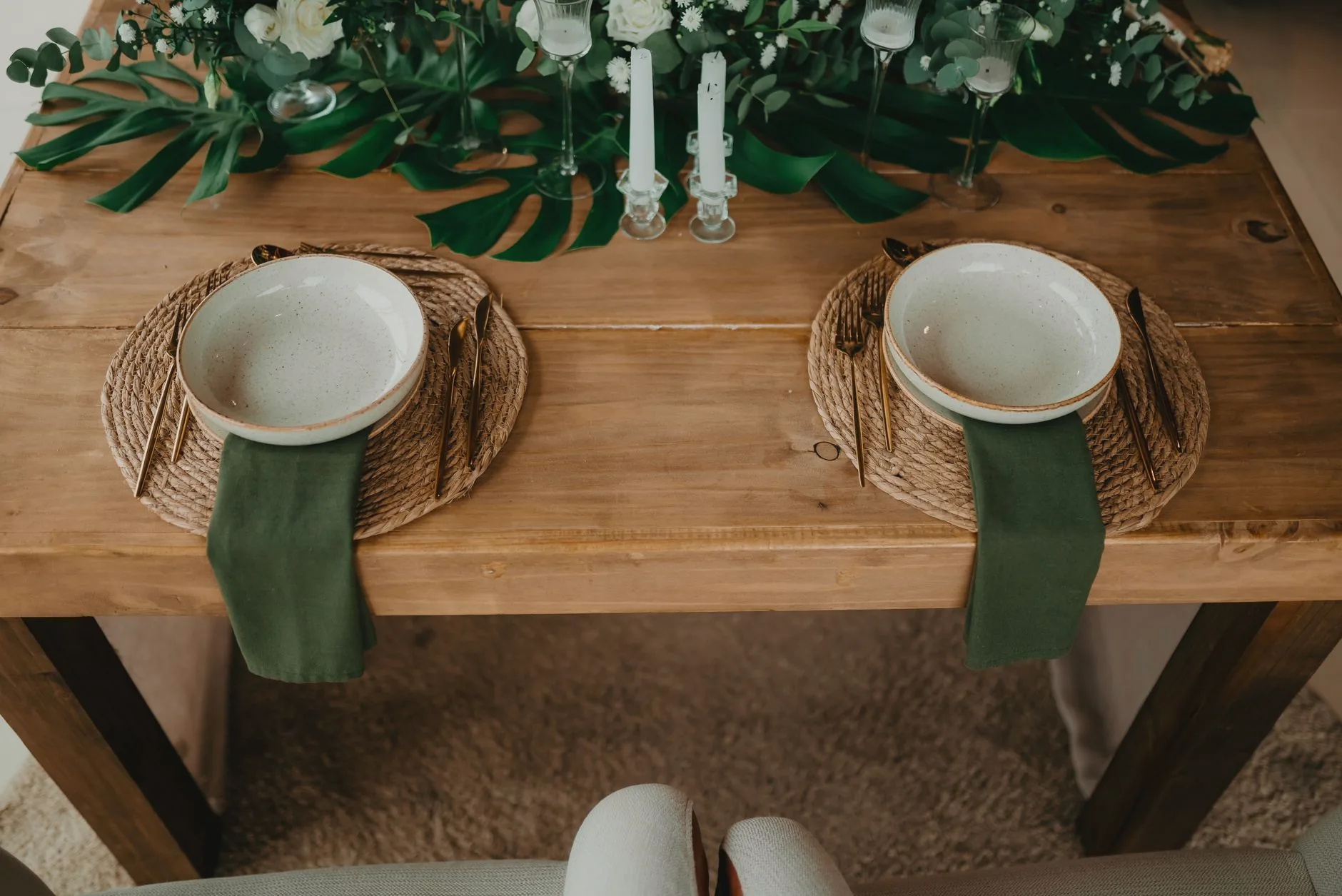 A rustic dining table set with two place settings and green decoration.