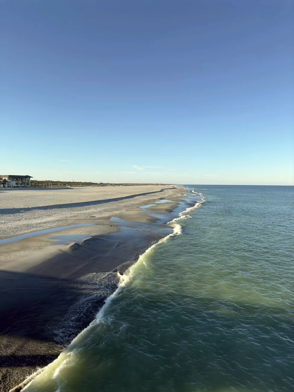 A wide view of St Augustine Beach, with calm waves beneath a clear blue sky.