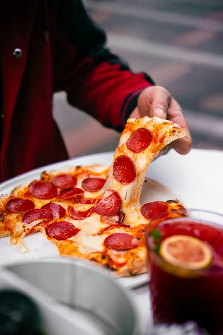 A hand pulls a slice of pepperoni pizza, with melted cheese stretching from it.