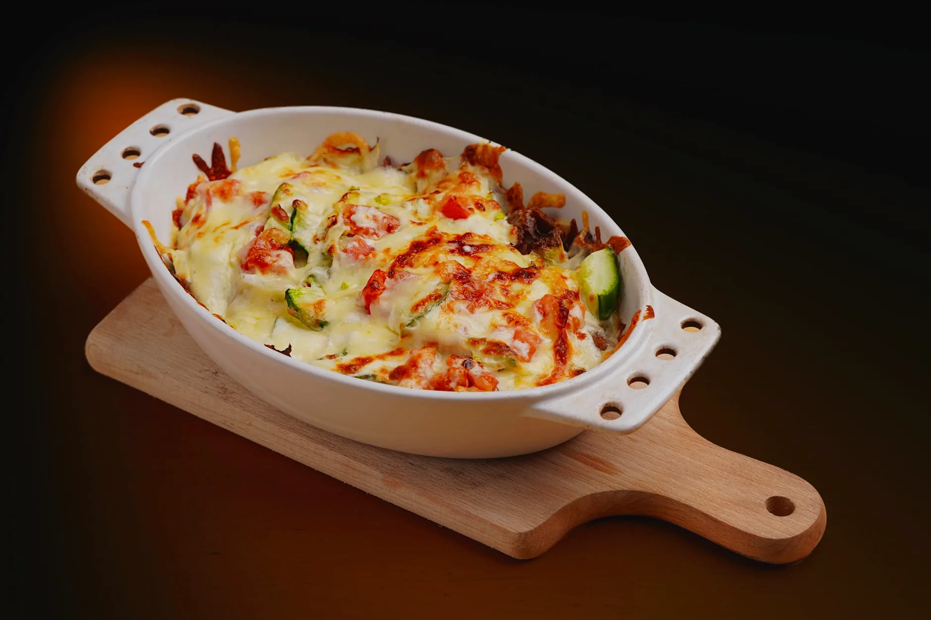 A baked vegetable gratin topped with cheese in a white dish.