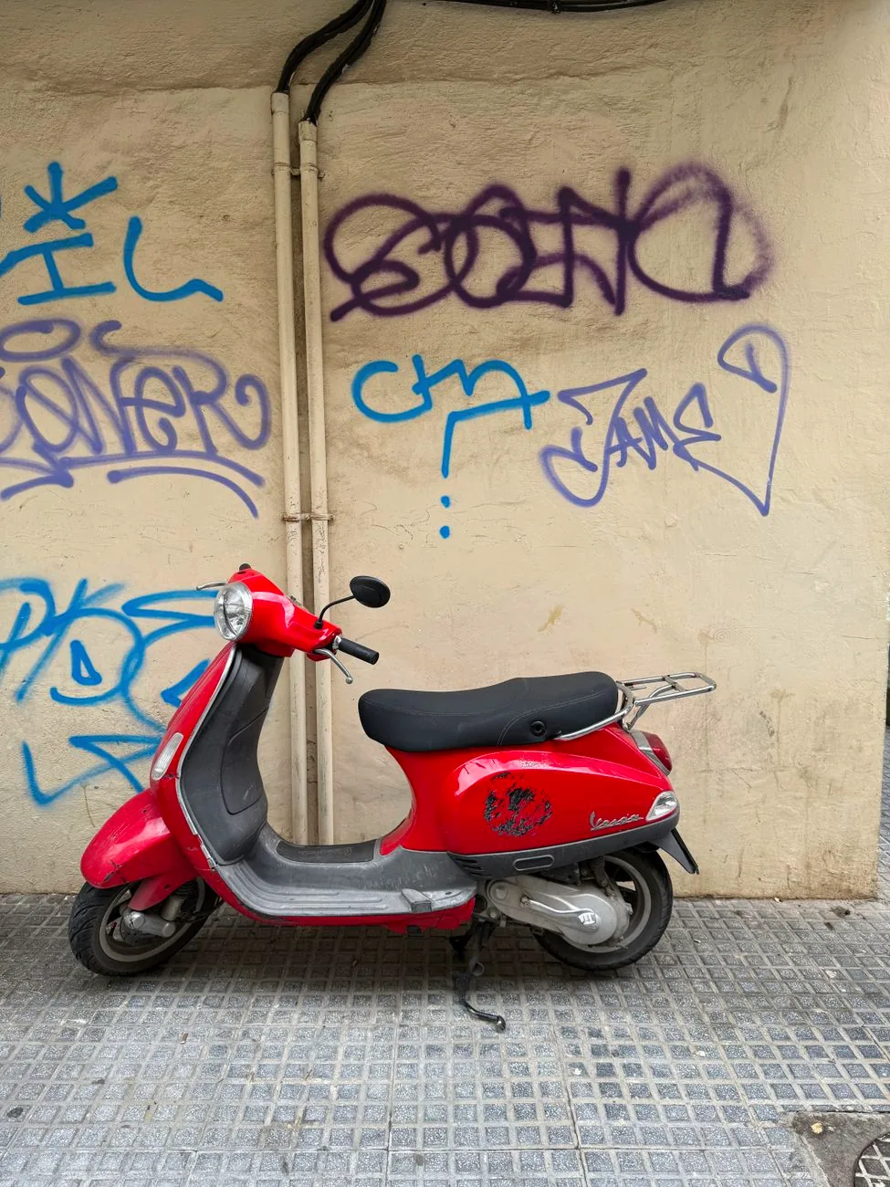 A red motor scooter parked beside a graffiti-covered wall in Málaga.