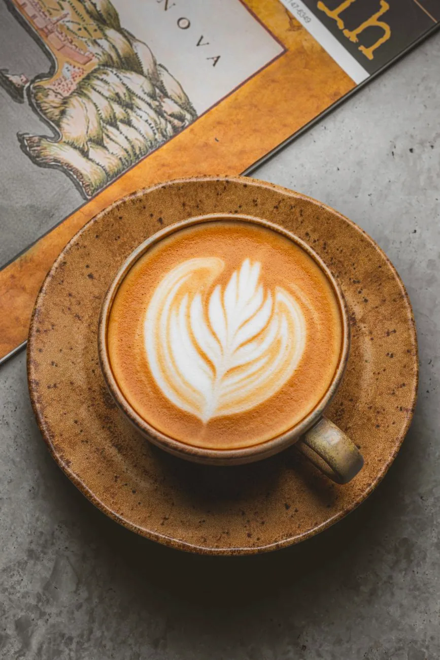 A latte in a rustic ceramic cup on a textured surface.