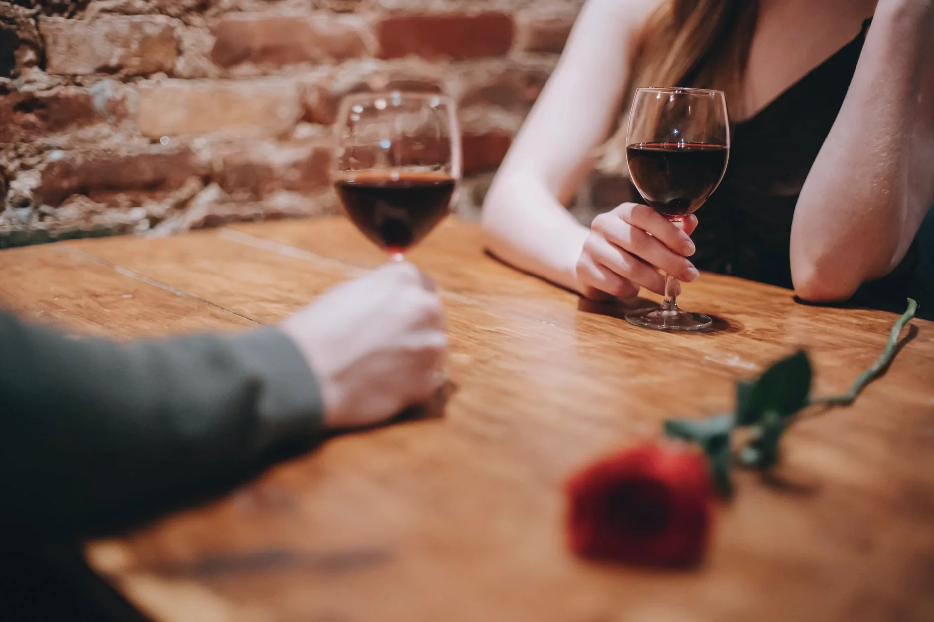 A couple share a table with wine and a red rose in a bar.