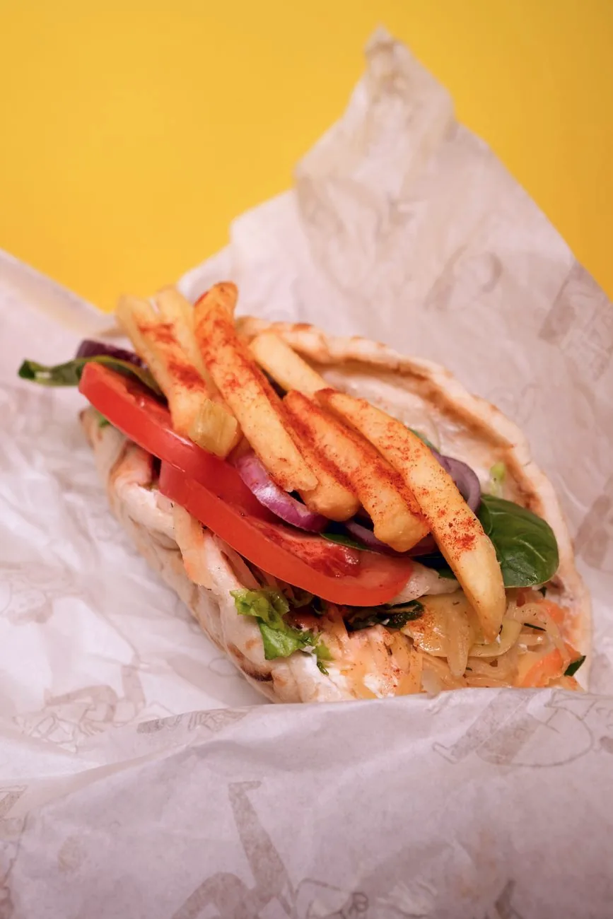 A gyro pita filled with meat, chips, tomato, red onion and greens.