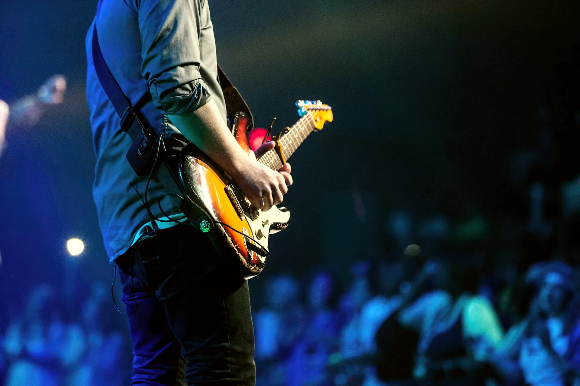 A guitarist playing an electric guitar on stage under concert lighting.