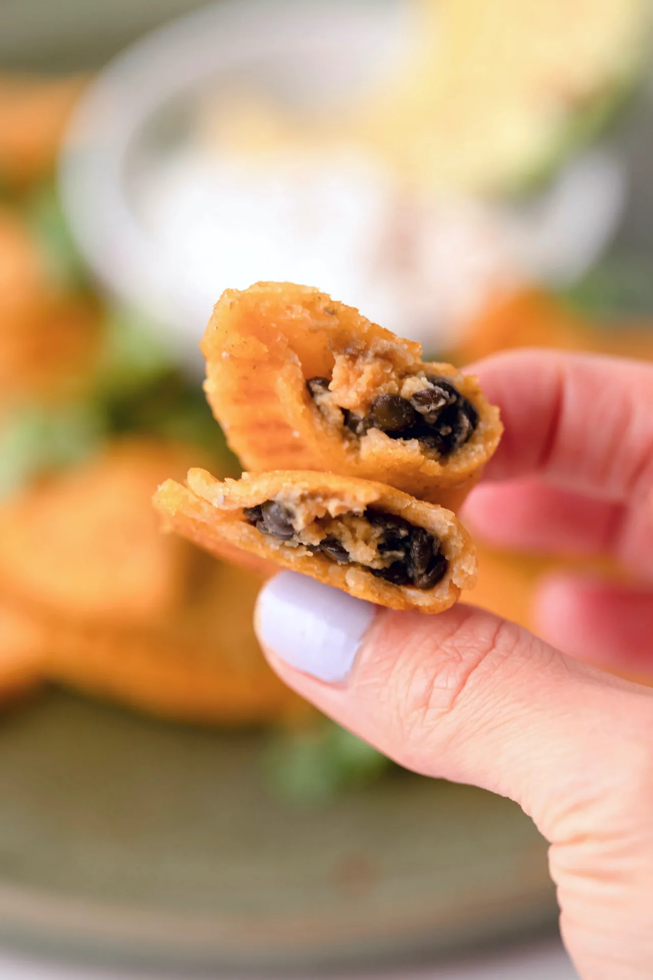 A hand holding a sweet potato empanada with lentil filling.