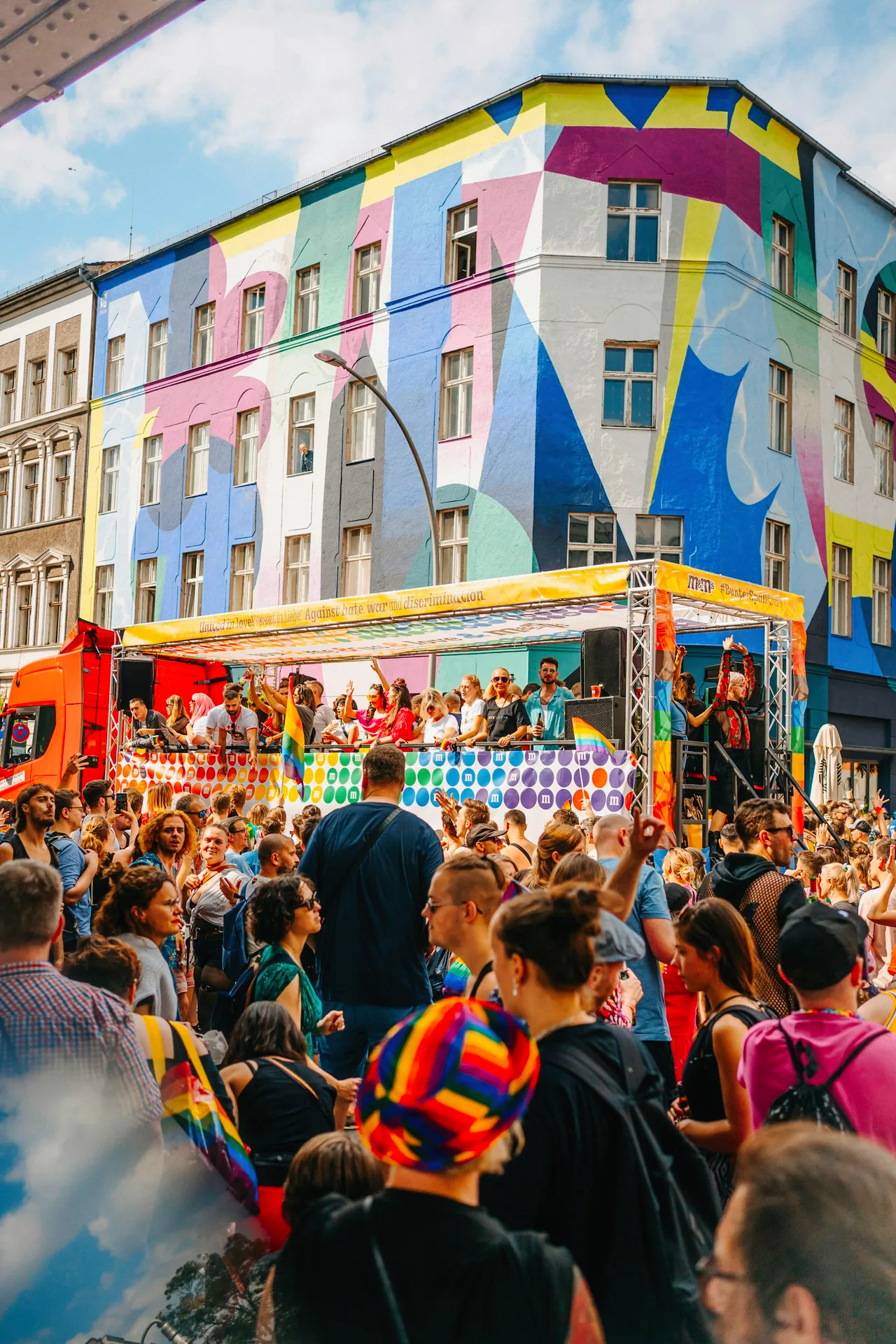 A crowd gathers outside a building with colourful windows at Berlin Pride 2022.