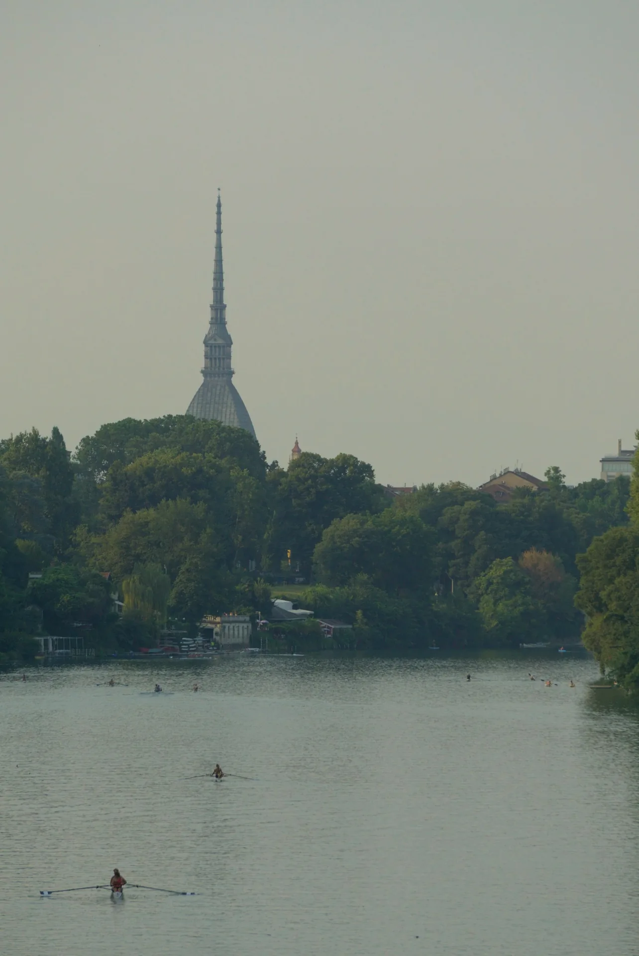 Canoes on the River Po with trees in Parco del Valentino and the Mole Antonelliana in the background.