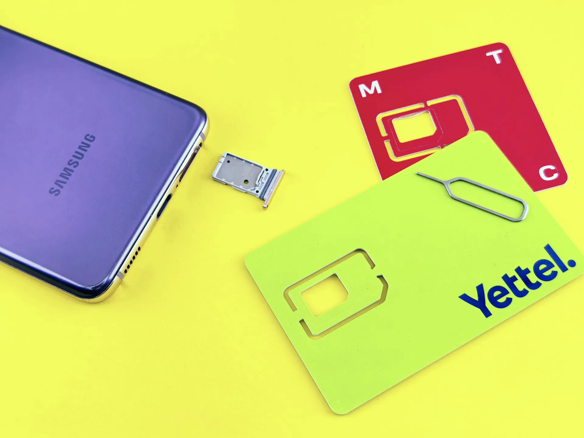 A purple smartphone, SIM tray and two SIM cards on a yellow surface